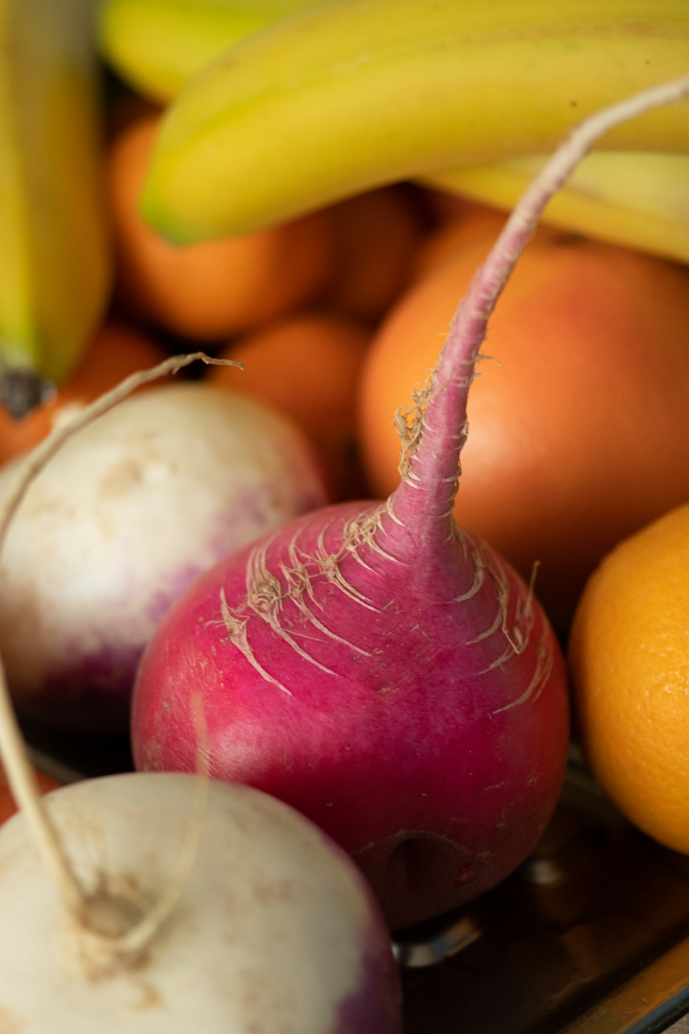 a close up of a radishes, oranges and bananas