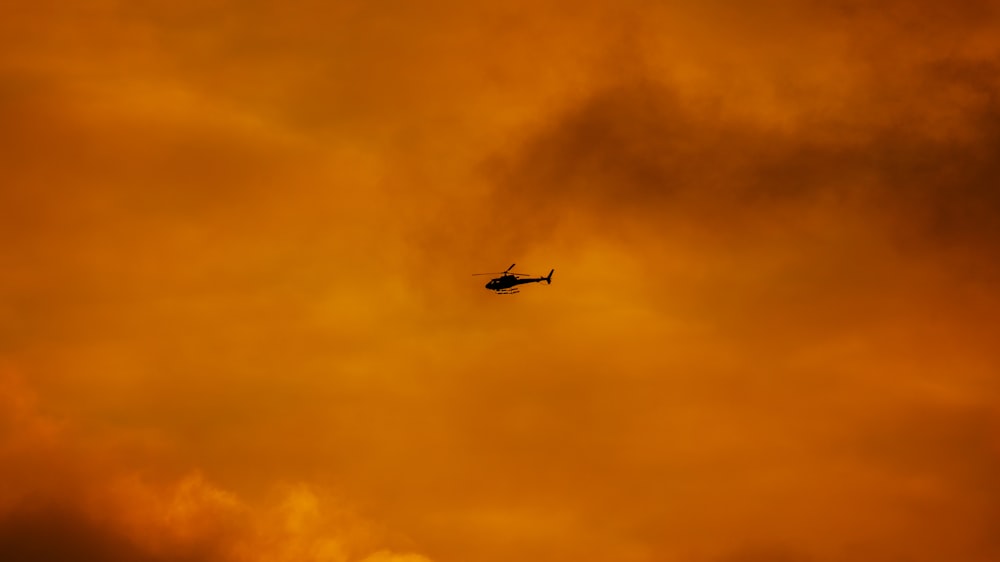 a helicopter flying through a cloudy orange sky