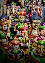A collection of colorful, intricately designed statues depicting various deities and figures from Indian mythology. The statues feature detailed carvings and vibrant colors, with elements representing traditional musical instruments and symbolic gestures.