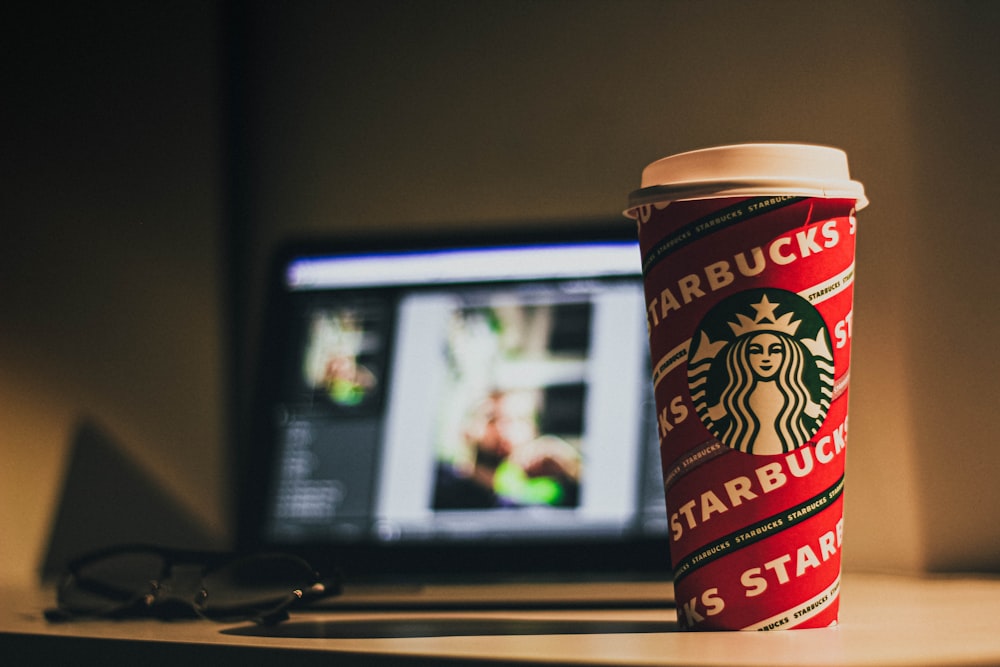 Eine Starbucks-Tasse auf einem Schreibtisch neben einem Computer