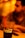 A clear glass with the Coca-Cola logo filled with a dark carbonated beverage and a red straw. In the background, a blurred figure is seated, creating a warm and cozy atmosphere with orange and yellow lighting.