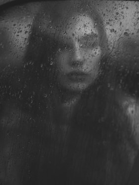 a black and white photo of a woman looking out a window