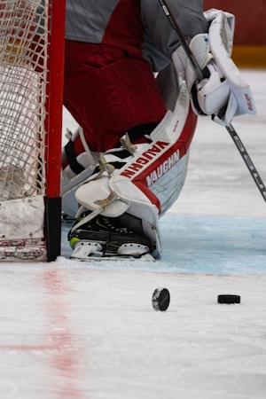 Hockey goaltender kneeling in front of the net between plays on a lit indoor rink