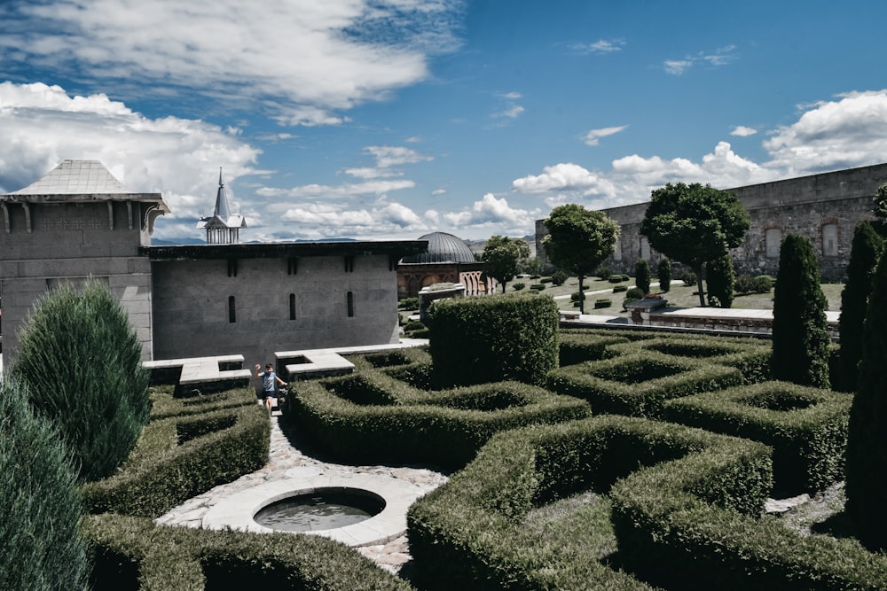 a maze in the middle of a garden with a building in the background