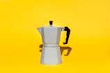 An elegant coffee maker on a white countertop with warm morning sunlight highlighting its orange details.