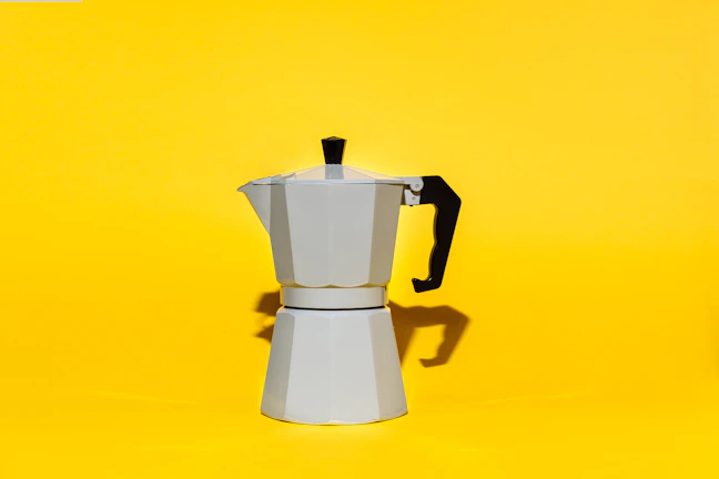 An elegant coffee maker on a white countertop with warm morning sunlight highlighting its orange details.