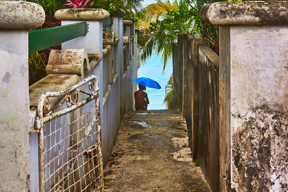 a person with a blue umbrella walking down a narrow alley way