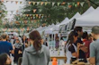Vibrant outdoor hemp market scene with smiling people browsing stalls under string lights.