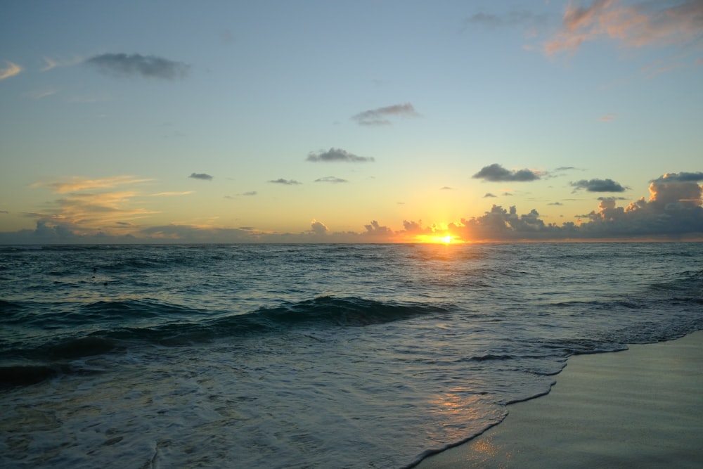 the sun is setting over the ocean on the beach