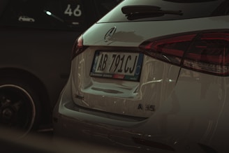 The rear view of a white Mercedes-Benz A35 AMG parked next to another vehicle. The vehicle's license plate is visible, and the Mercedes-Benz logo is prominently displayed. The taillights are sleek and modern, matching the car's sporty aesthetic.