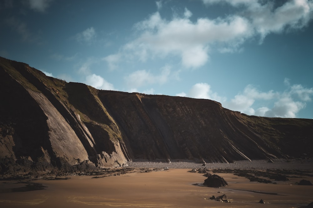 a sandy beach next to a cliff under a cloudy sky