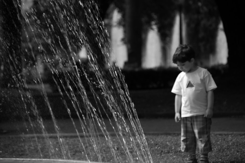 a young boy standing in front of a sprinkle fountain