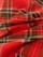 A close-up view of a red and green plaid fabric with intersecting lines and patterns. The material appears to be soft, possibly flannel, with multiple layers creating subtle folds and shadows.