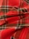 A close-up view of a red and green plaid fabric with intersecting lines and patterns. The material appears to be soft, possibly flannel, with multiple layers creating subtle folds and shadows.