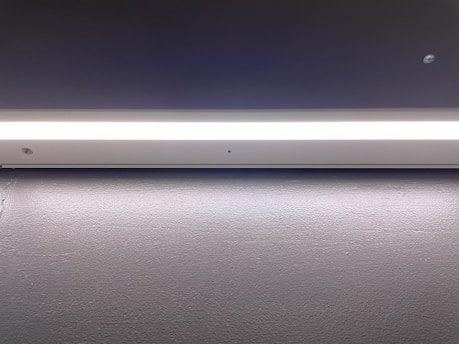 A minimalistic and modern light fixture is mounted on a smooth, dark surface. The lighting strip provides a bright, even illumination along its entire length, casting a subtle glow onto the surface below.