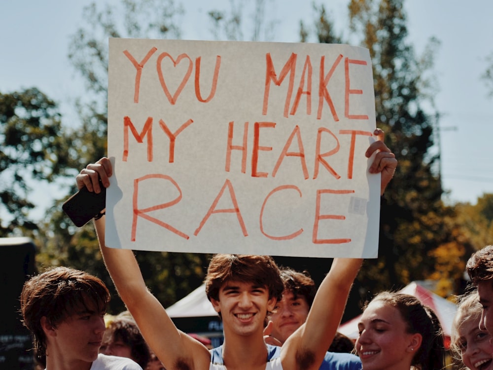 a man holding a sign that says you make my heart race