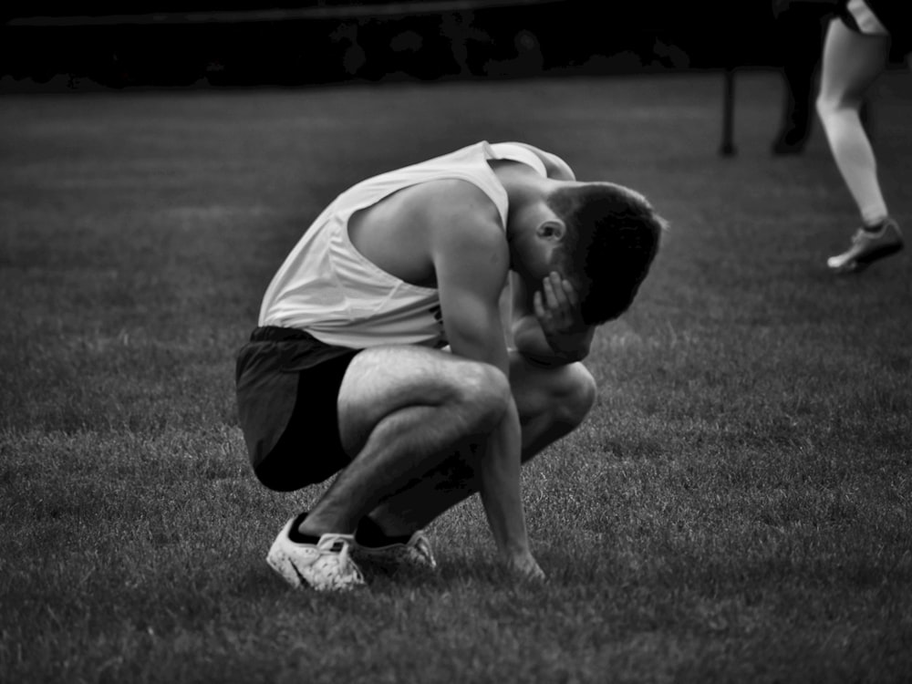 a man kneeling down in the grass with his head in his hands