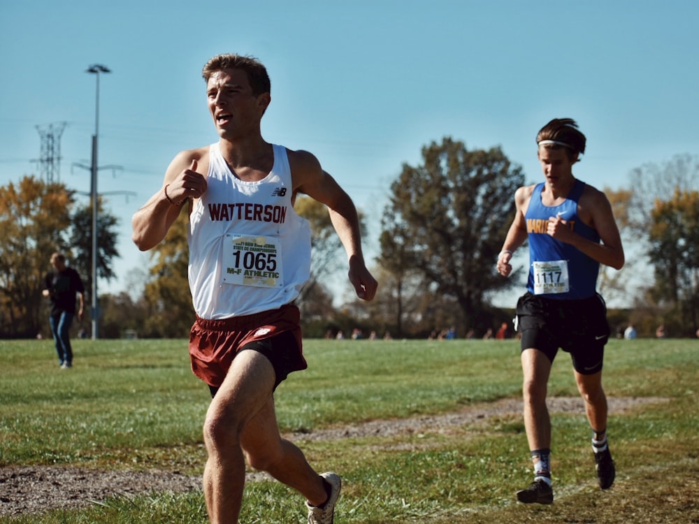 a couple of men running across a grass covered field