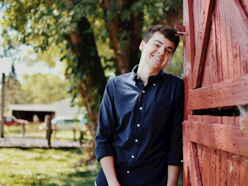 a young man leans against a red barn door