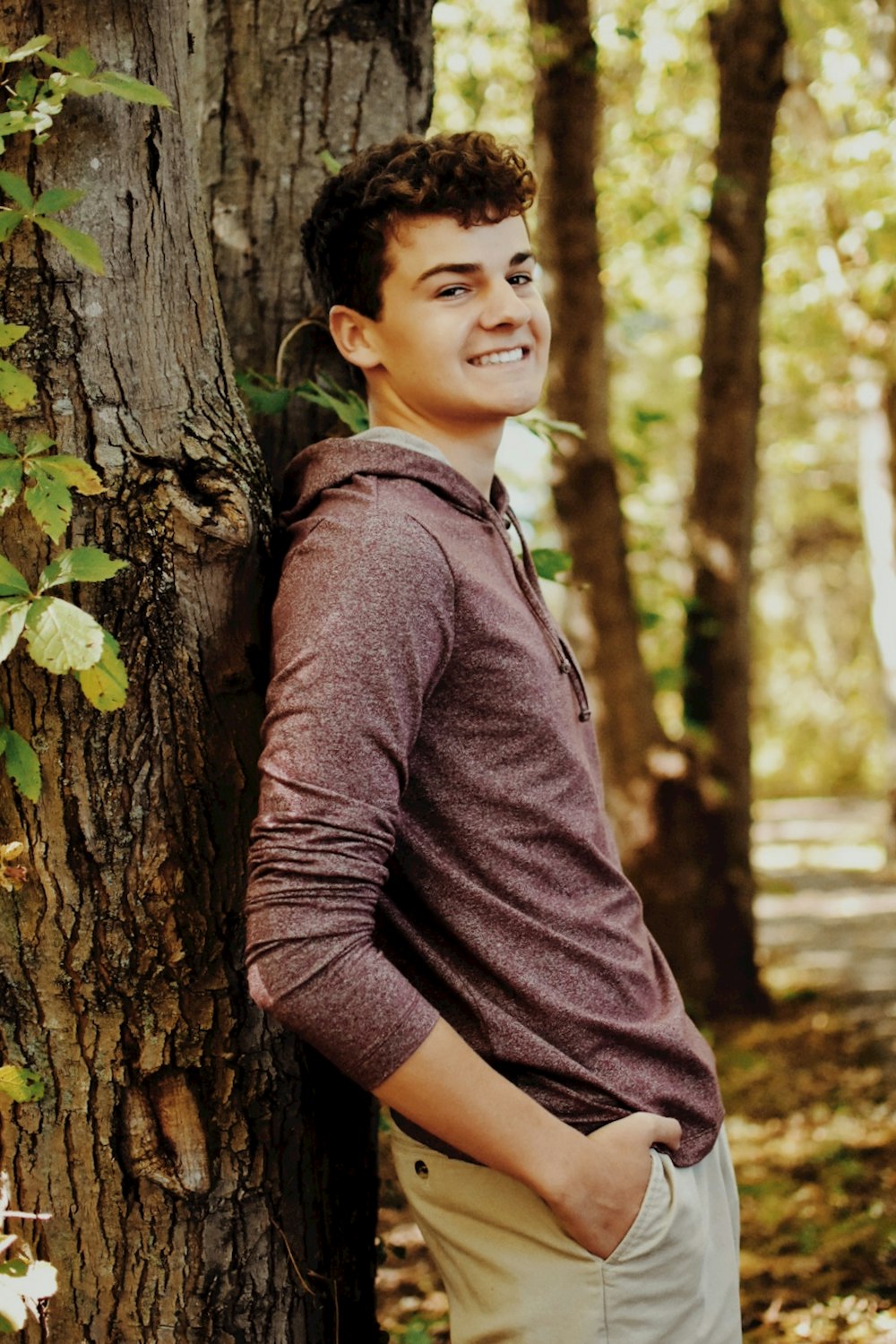 a young man leaning against a tree in the woods