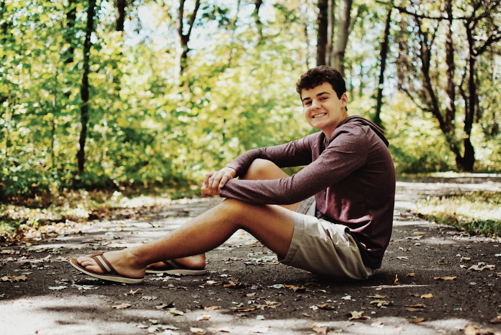 a young man sitting on a road in the woods