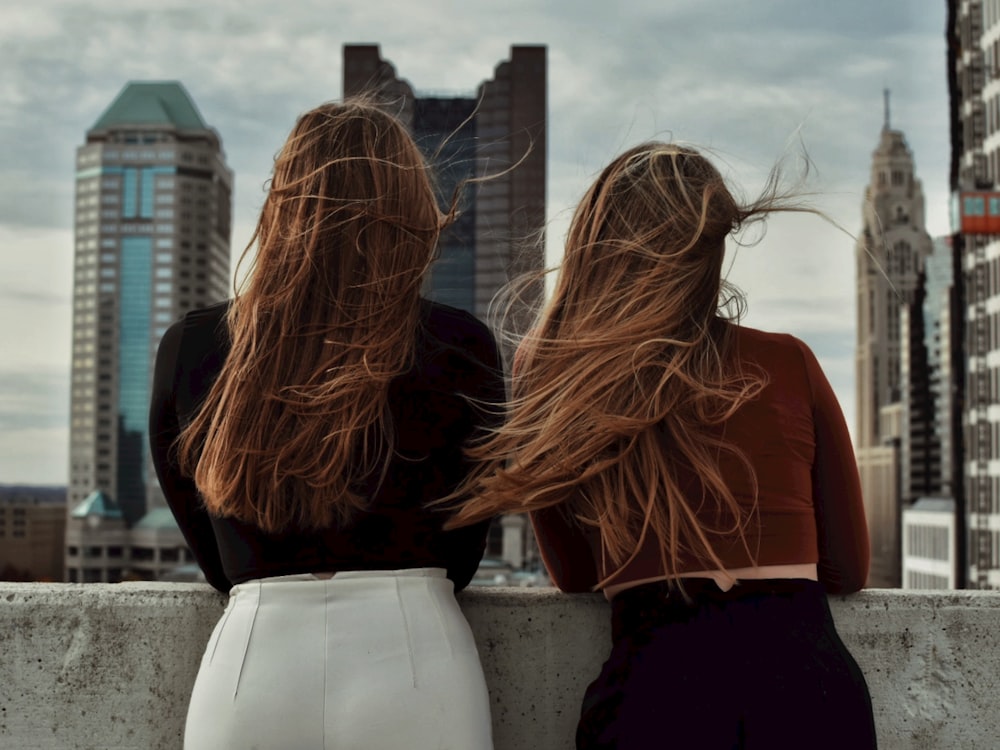 two women with long hair sitting on a ledge