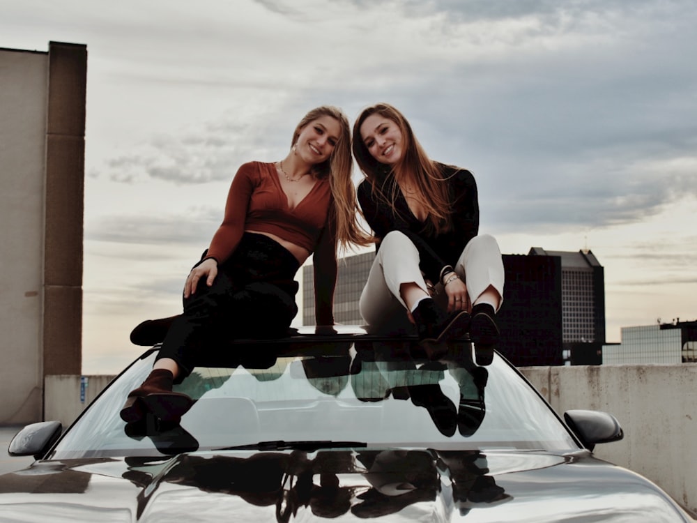 two women sitting on the hood of a car