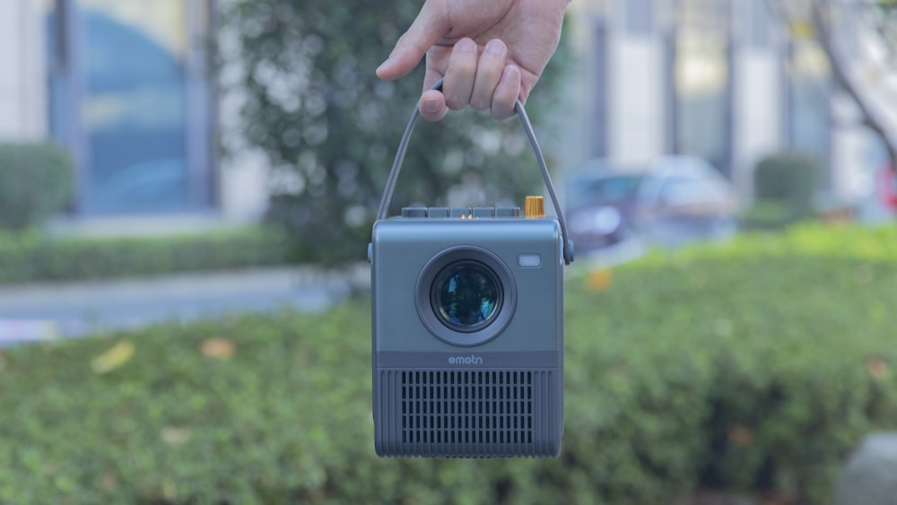 a hand holding a small camera in front of a building