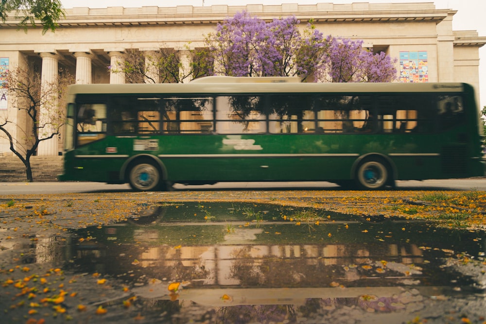 a green bus driving down a street next to a tall building