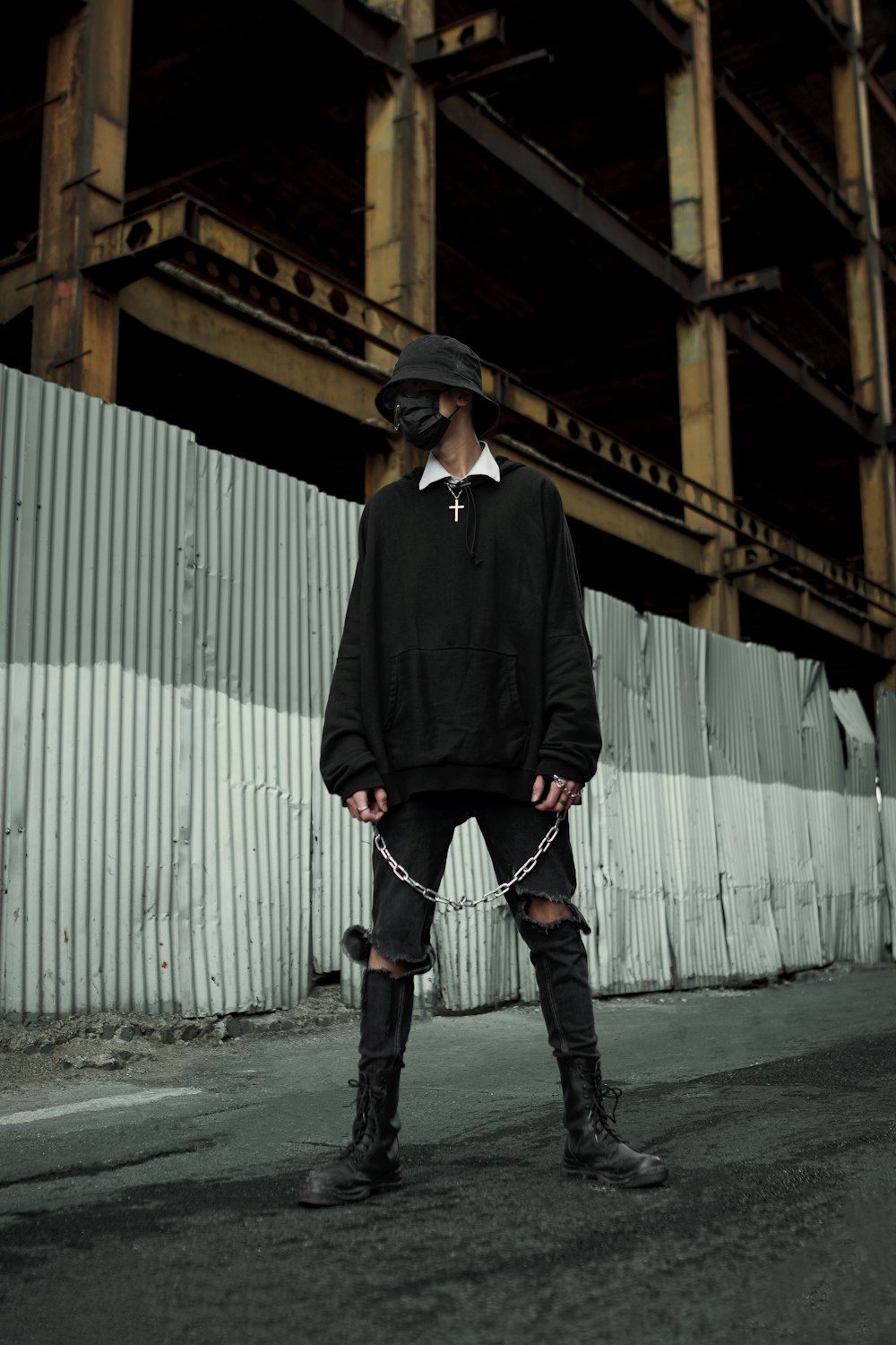 a man in a black hoodie and black boots standing in front of a building