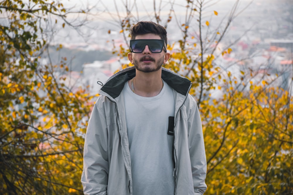 a man standing in front of a tree wearing a pair of sunglasses