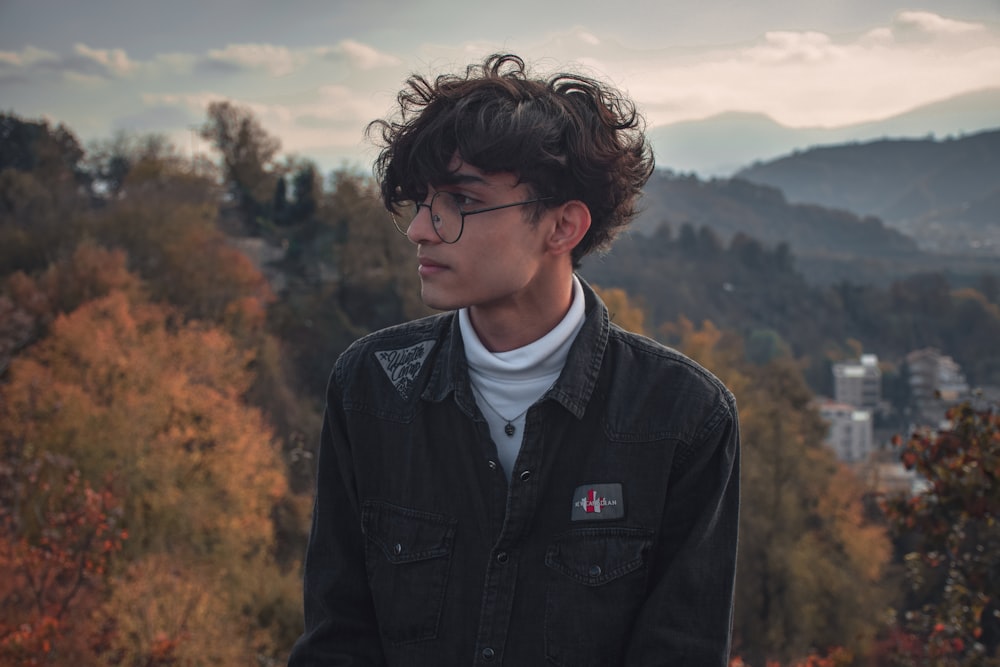 a young man with glasses standing in front of a mountain