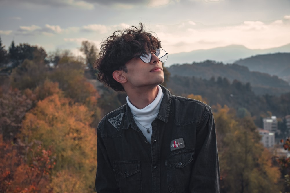 a man with glasses standing in front of a mountain