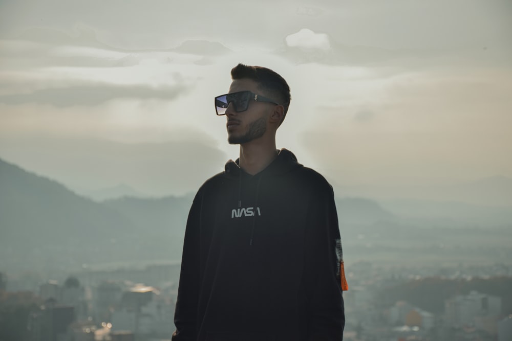 a man in a hoodie and sunglasses standing in front of a cityscape