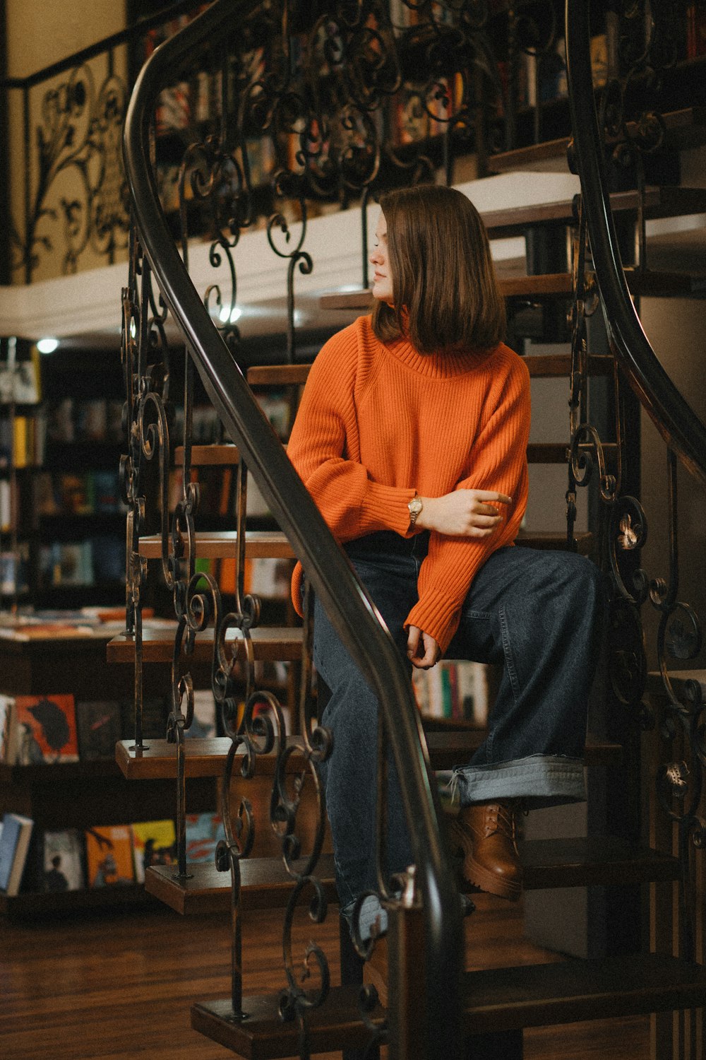 a woman in an orange sweater is sitting on a set of stairs