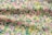 A fabric covered with a dense, colorful floral pattern featuring a variety of small flowers in pink, purple, yellow, and blue hues against a green background.