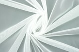 A close-up view of white, translucent fabric arranged in a swirling pattern. The intricate texture of the mesh is visible, creating a delicate and airy appearance.