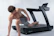 A man mid-sprint on a treadmill, sweat glistening, surrounded by sleek gym equipment.