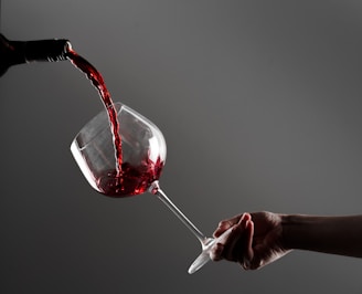 a hand holding a wine glass with red wine being poured into it