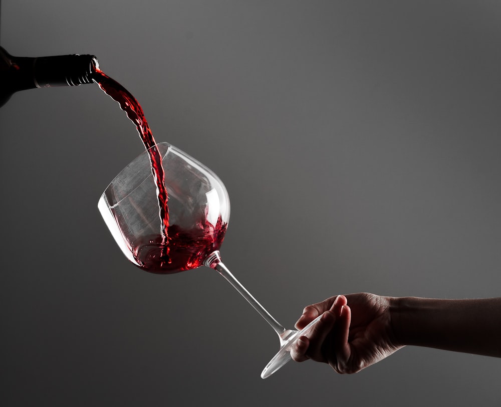 a hand holding a wine glass with red wine being poured into it
