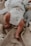 A newborn baby is lying on a soft, textured beige blanket. The baby is wearing a white diaper with the words 'respect nature' and a small plant graphic. Next to the baby is a plush toy resembling an animal dressed in a striped outfit.