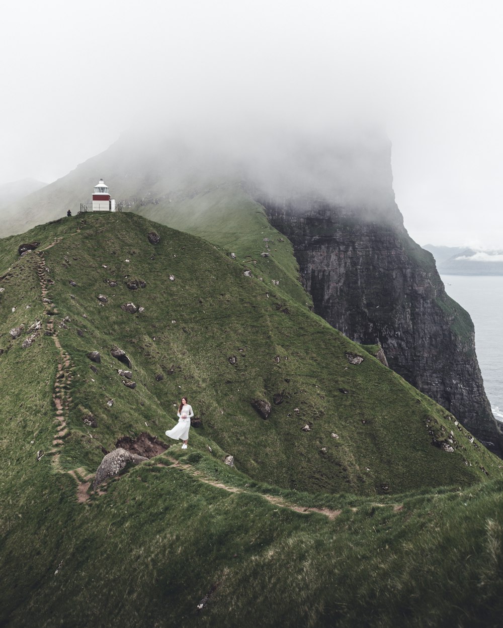a bride and groom standing on a grassy hill with a lighthouse in the background