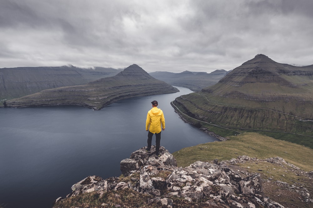 a man in a yellow jacket is standing on a rock