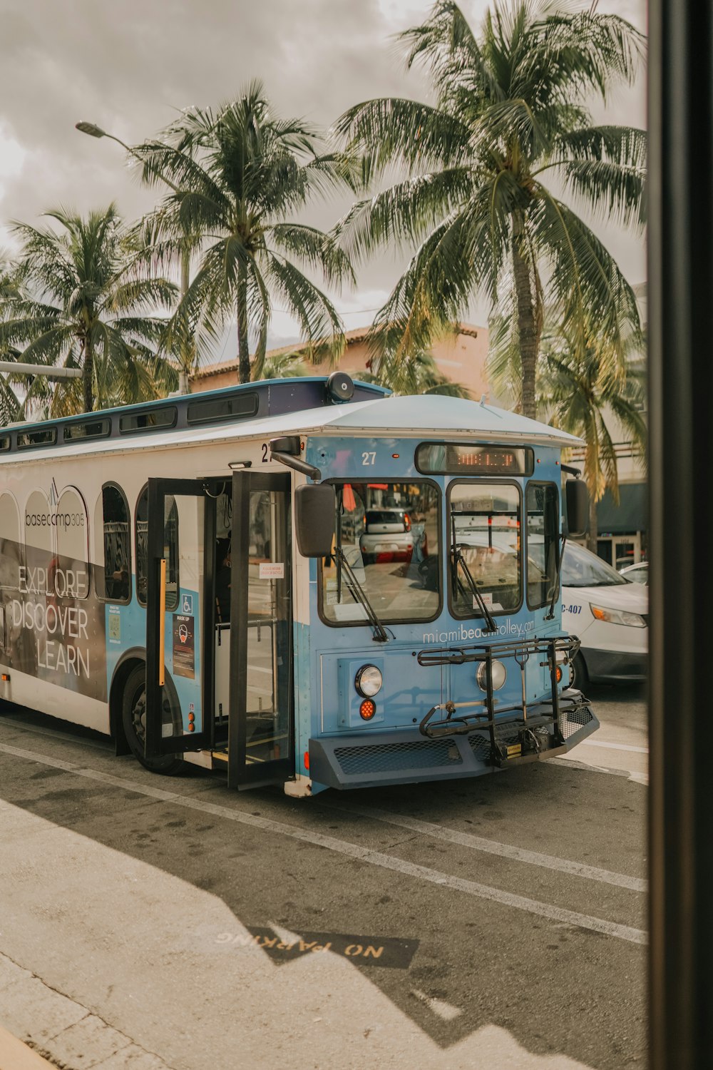 a blue and white bus driving down a street next to palm trees