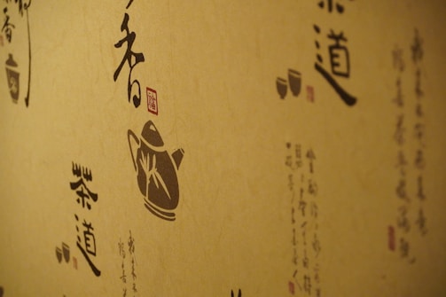 A wall decorated with artistic calligraphy and traditional illustrations, featuring a silhouette of a teapot and stylized Asian scripts. The designs are rendered in dark shades on a natural beige background, conveying a traditional and cultural aesthetic.