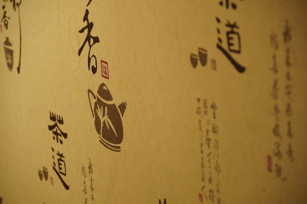 A wall decorated with artistic calligraphy and traditional illustrations, featuring a silhouette of a teapot and stylized Asian scripts. The designs are rendered in dark shades on a natural beige background, conveying a traditional and cultural aesthetic.