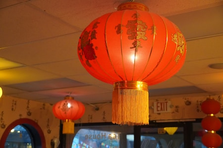 A series of traditional red Chinese lanterns hanging inside a room, with calligraphy visible on the walls. The lanterns are adorned with gold tassels and Chinese characters.