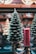 A decorative candle shaped like a Christmas tree is placed alongside a cylindrical red candle with a textured surface. Both are set on ornate metal holders with intricate scrollwork. The background features blurred holiday décor, creating a festive atmosphere.