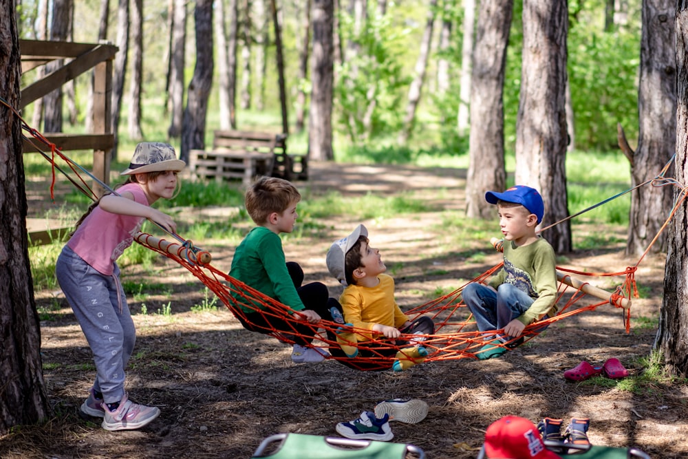 a group of kids sitting in a hammock in the woods
