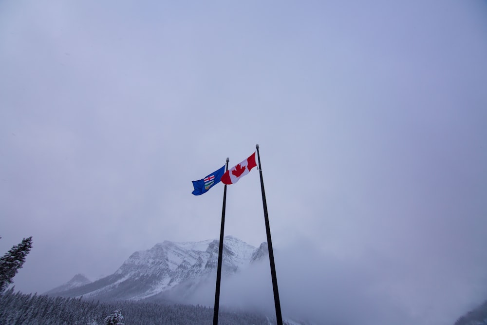 two canadian and canadian flags on poles in front of a mountain